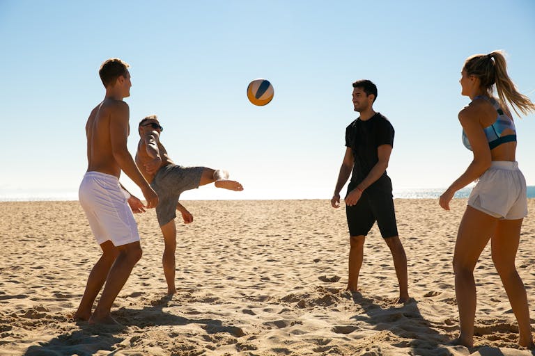 Four adults enjoying a game of beach volleyball under a clear blue sky.